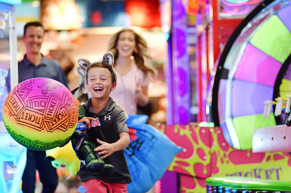 Child playing with colorful ball in arcade game area with neon lights and entertainment machines