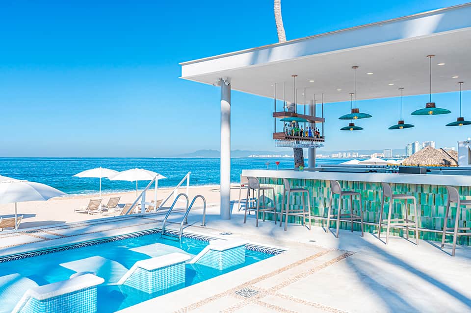 Modern beachfront bar and pool with white canopy, green seating, ocean views