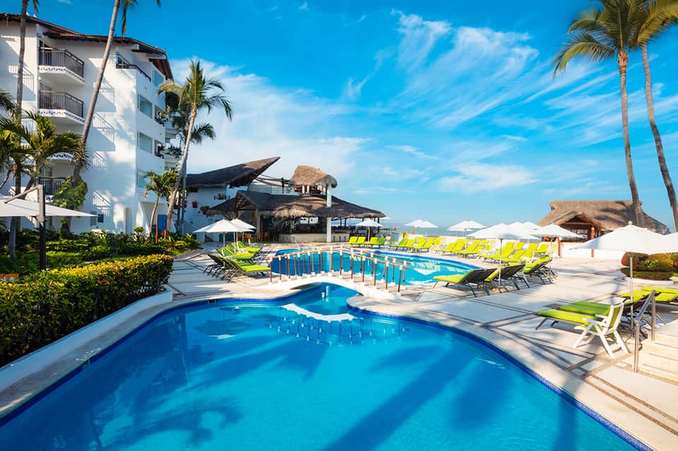 Luxury beachfront resort pools with bright yellow lounge chairs, thatched palapas, and palm trees by ocean