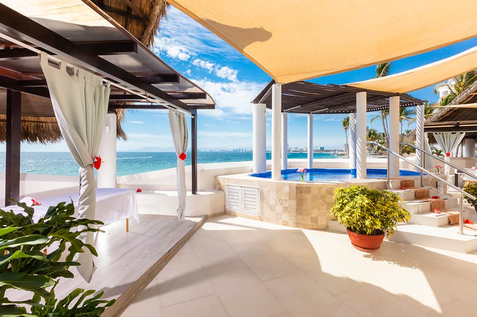 Beachfront cabana with white columns, cream curtains, blue pool, and ocean vista