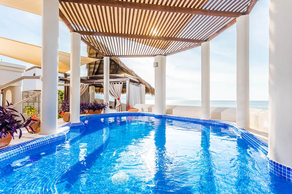 Covered beachfront pool with blue mosaic tiles and ocean view through columns