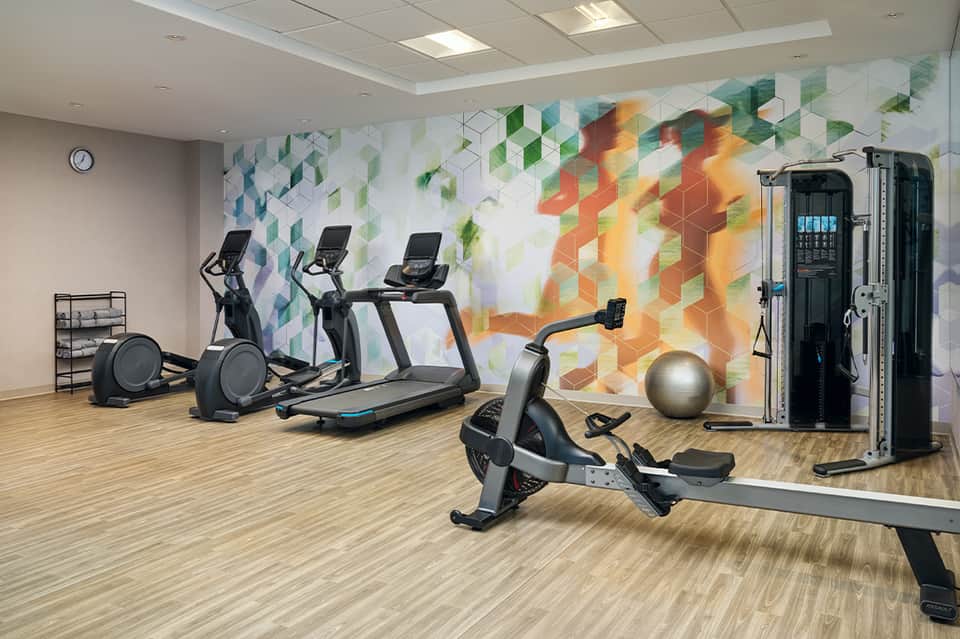 Modern fitness center with treadmills, stationary bikes, colorful geometric wall mural, and exercise equipment