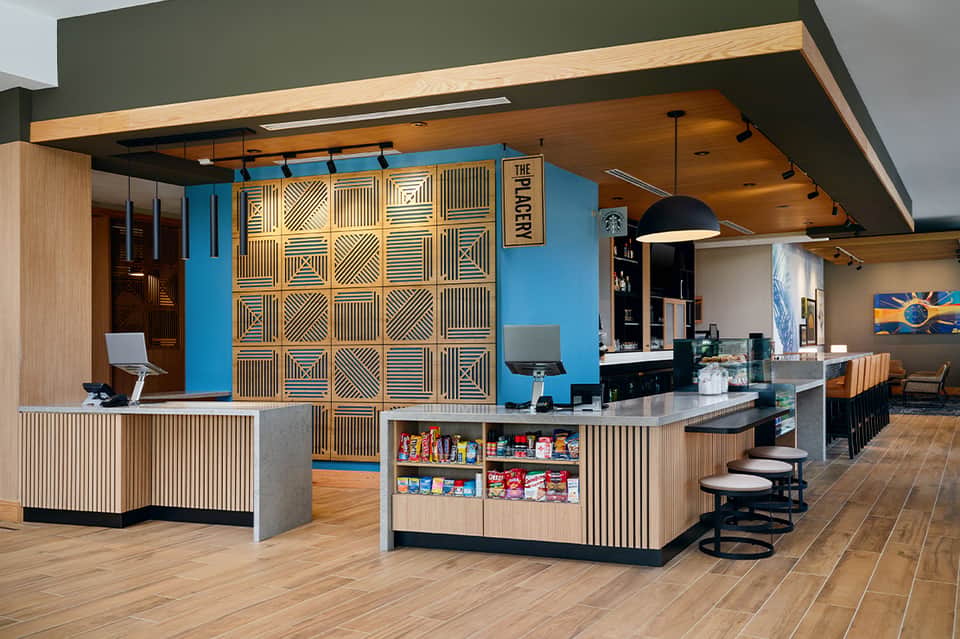 Contemporary hotel café with blue accent wall, wooden geometric feature wall, counter service, and modern seating