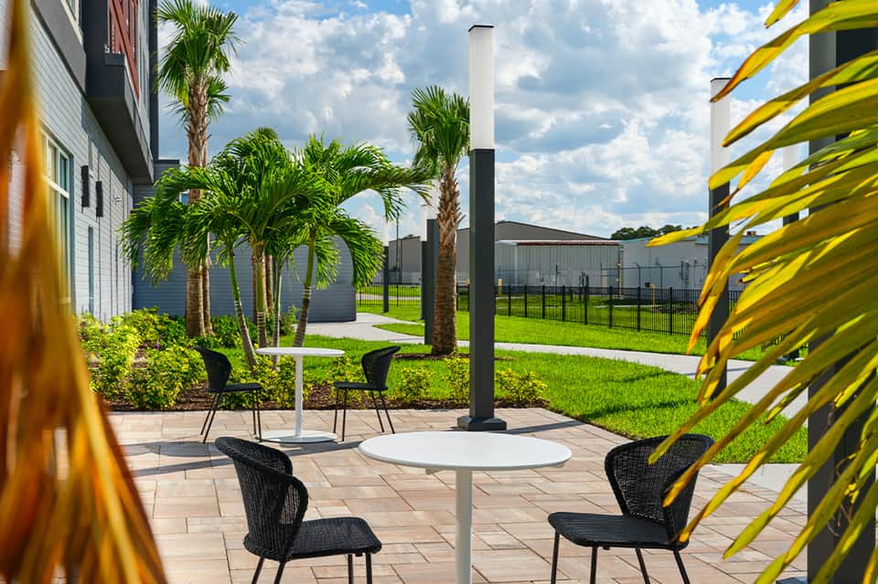 Outdoor seating area with black chairs, white tables, palm trees, and yellow architectural elements