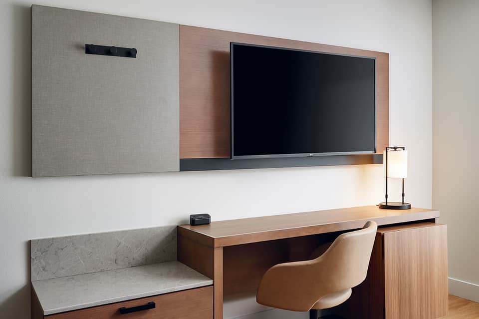 Modern hotel desk with wall-mounted TV, wood frame, desk chair, and minimalist design