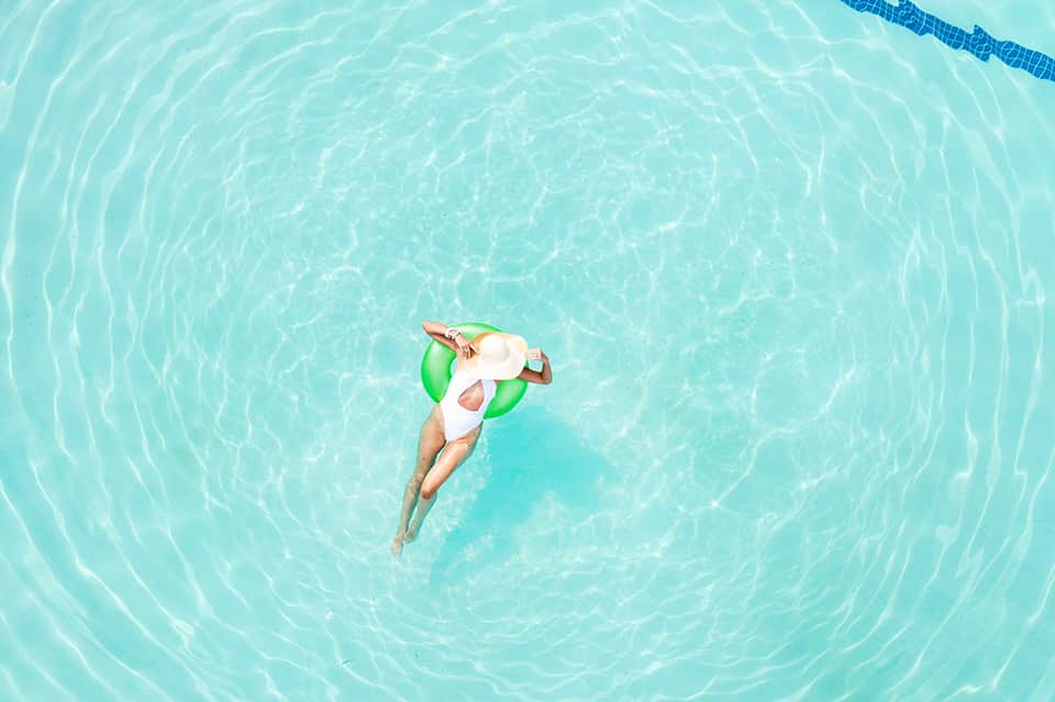 Aerial view of woman floating on green inflatable in crystal-clear turquoise pool
