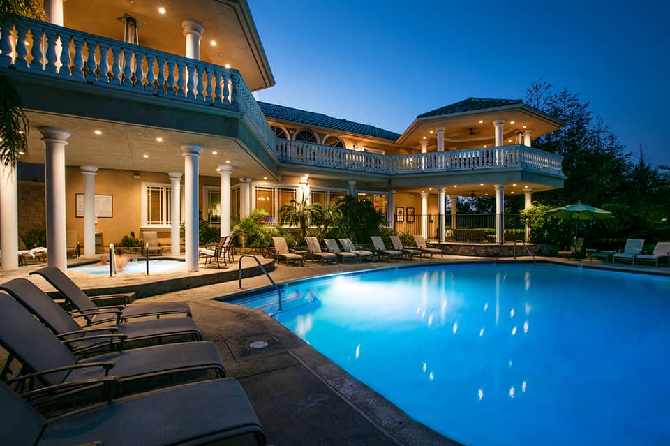 Luxury home with illuminated pool, columns, balconies, and lounge seating at night