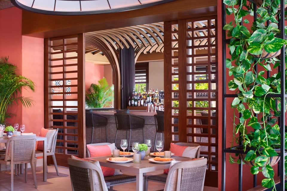Modern dining area with red accent walls, wooden lattice screens, and outdoor patio access