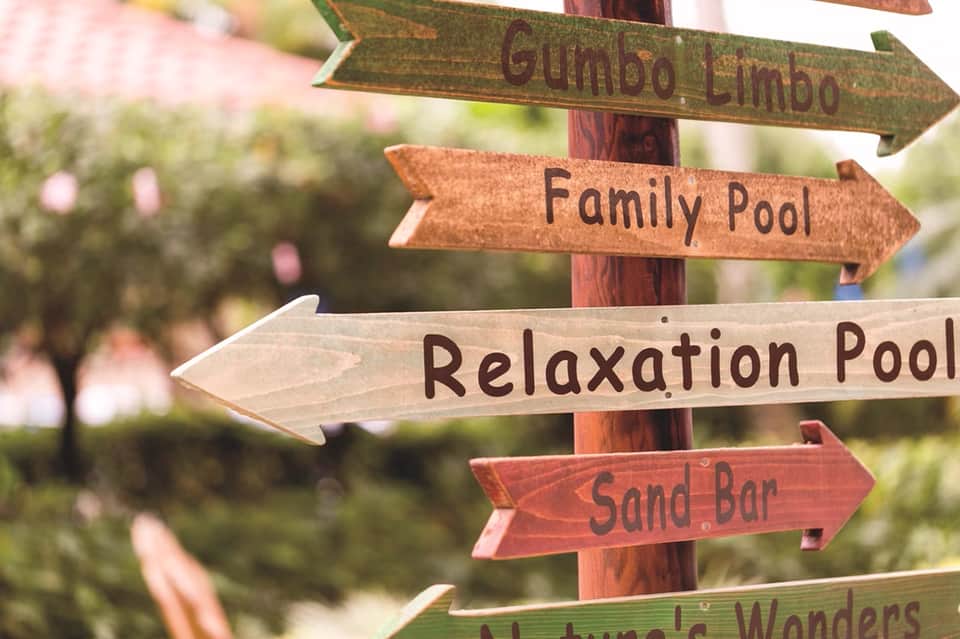 Rustic wooden directional signs pointing to family pool, relaxation pool, sand bar