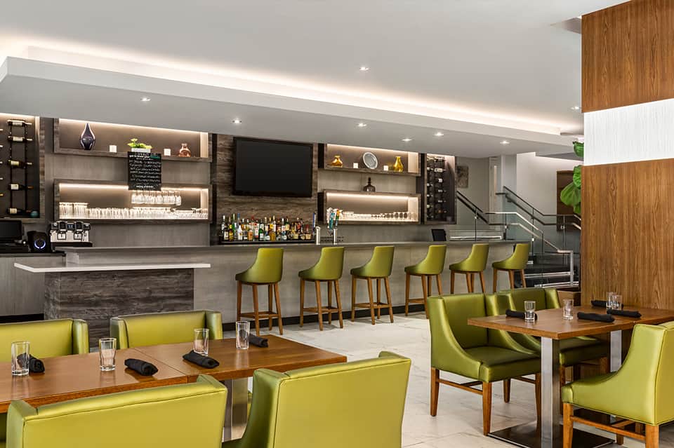 Modern hotel bar lounge with lime green seating, wood accents, and contemporary bar counter