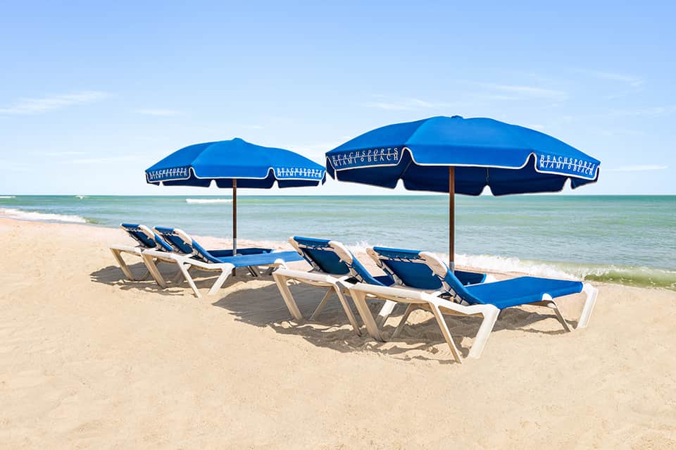 Beach setup with blue loungers and umbrellas branded with 'Beach Sports' on sandy shore