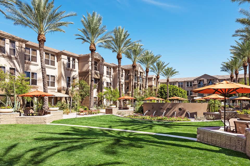 Resort courtyard with palm trees, green lawn, orange umbrellas, and apartment buildings