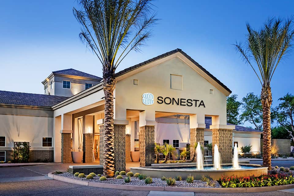 Sonesta hotel entrance at dusk with illuminated signage, palm trees, and modern architectural design