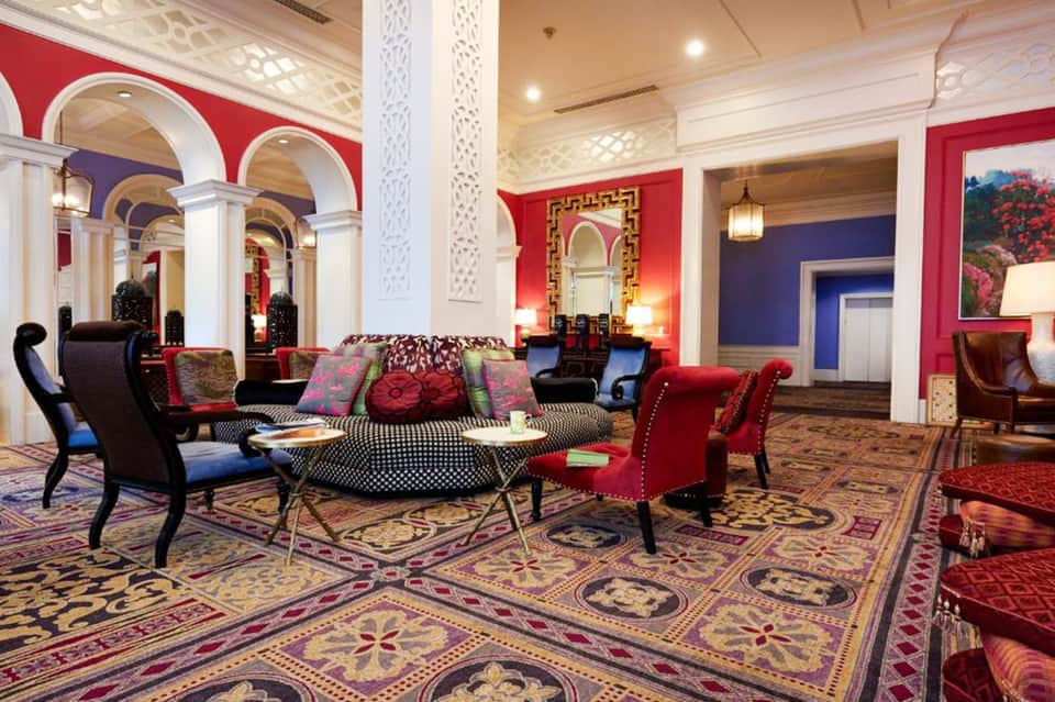 Luxurious hotel lobby with bold red walls, colorful seating, decorative columns, and ornate patterned flooring
