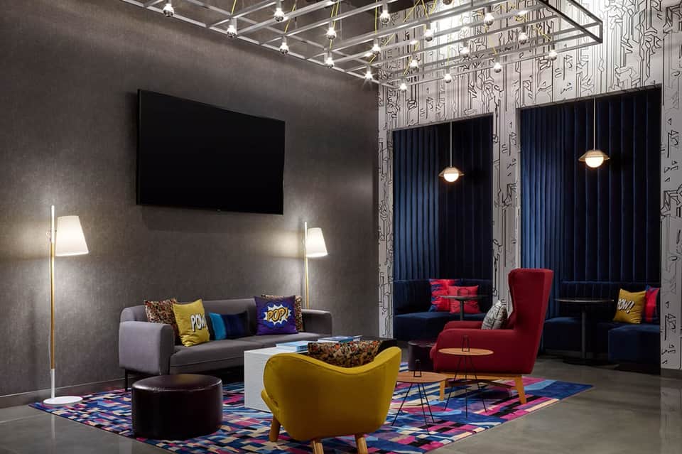 Modern hotel entertainment lounge with colorful seating, TV, patterned walls, and curtains