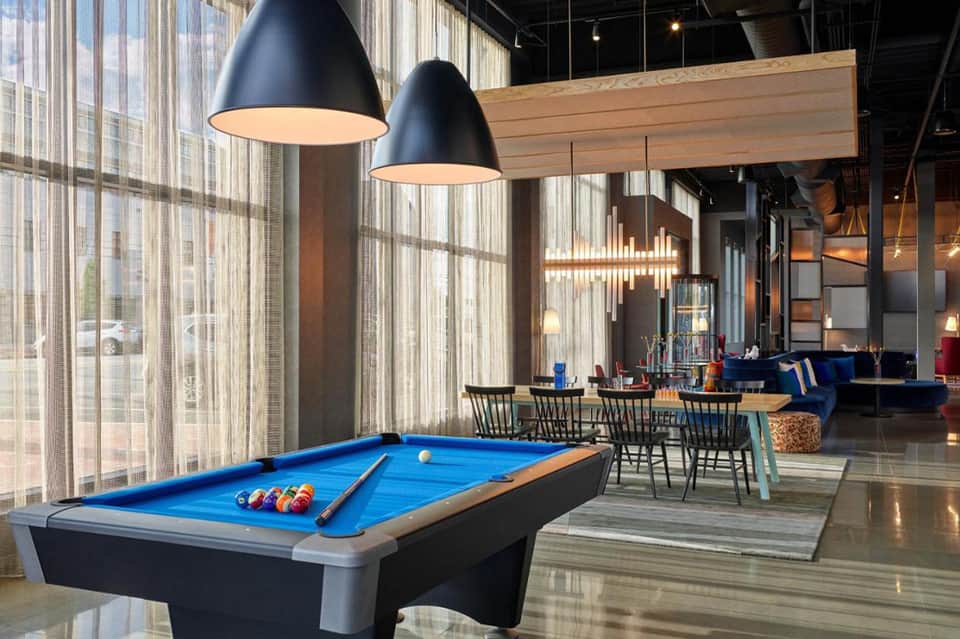 Contemporary lounge with pool table, pendant lights, blue accents, and floor-to-ceiling windows
