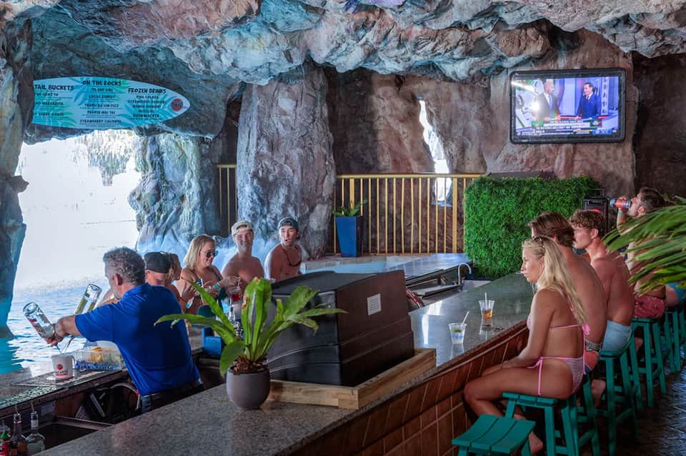 Cave bar built into natural rock formation overlooking ocean, guests seated at bar counter