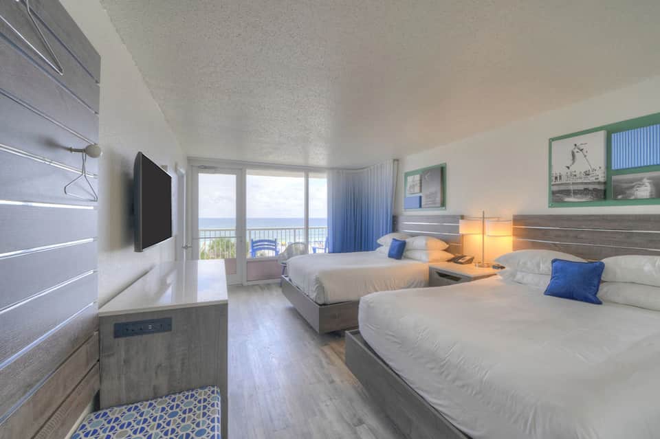Beachfront hotel room with twin beds, ocean view balcony, flat-screen TV, and blue accents