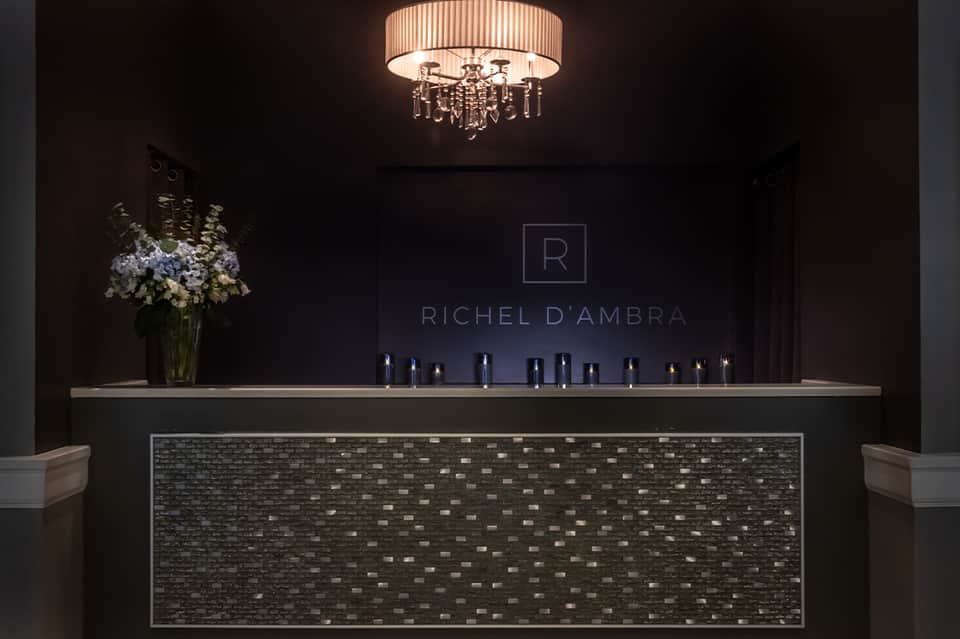 Luxury spa reception desk with dark brick detail, elegant chandelier, and flower arrangement