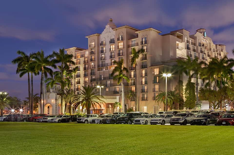 Illuminated multi-story resort hotel at dusk with palm trees and manicured grounds