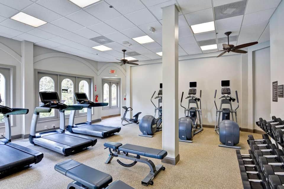 Bright fitness center with treadmills, ellipticals, and dumbbells near glass doors