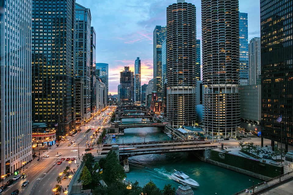 Chicago River cityscape at dusk with illuminated skyscrapers and bridges reflected in water