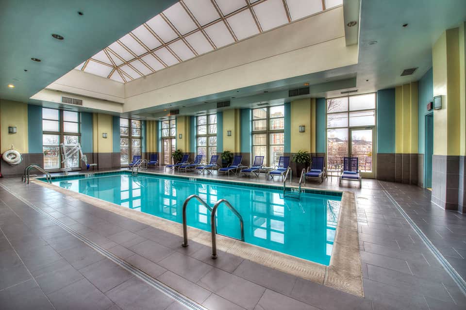 Indoor pool with turquoise water, skylight ceiling, and blue lounge chairs along side