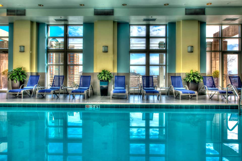 Indoor pool with blue loungers, large windows, yellow and turquoise walls, city view in background