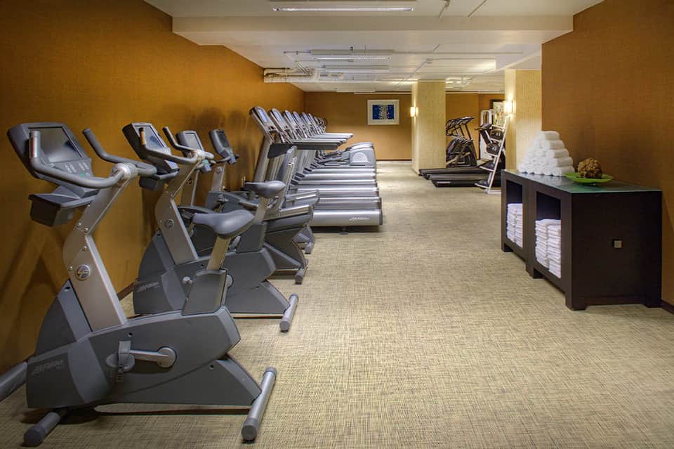 Fitness center with stationary bikes, ellipticals, and treadmills against golden yellow walls
