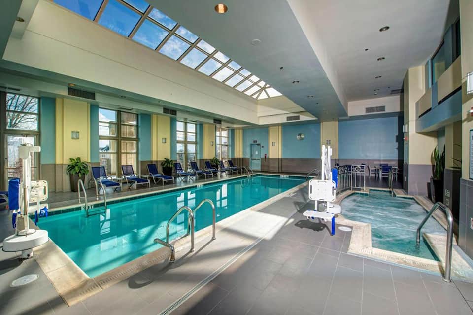 Indoor heated pool with skylight ceiling, lounge chairs, and spa hot tub in bright room