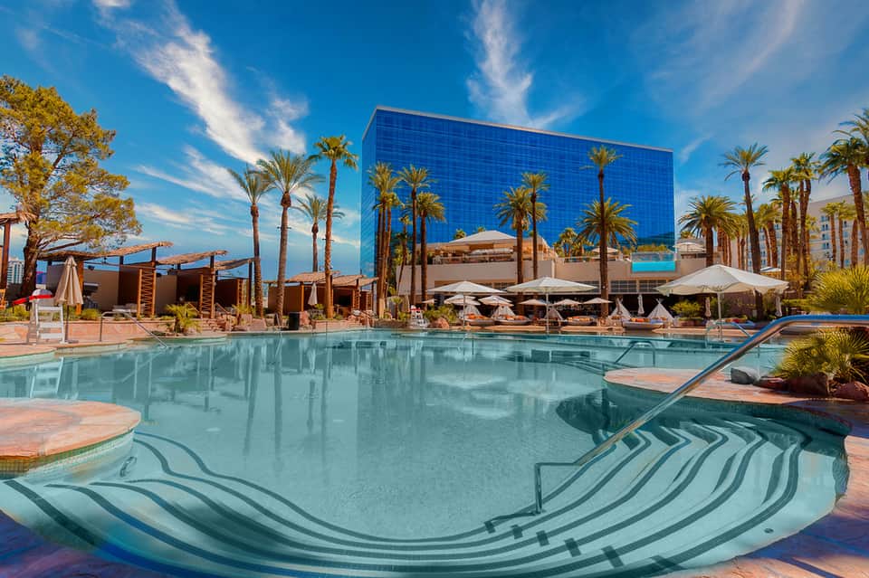 Modern resort pool with geometric tile design, palm trees, and contemporary blue glass building