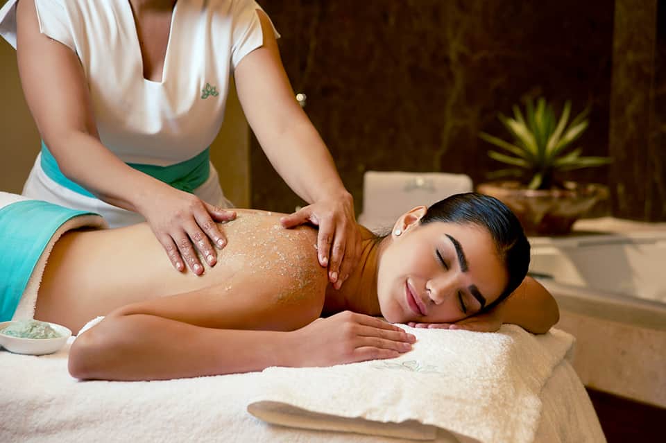 Spa therapist applying exfoliating scrub treatment to client's back during massage therapy session