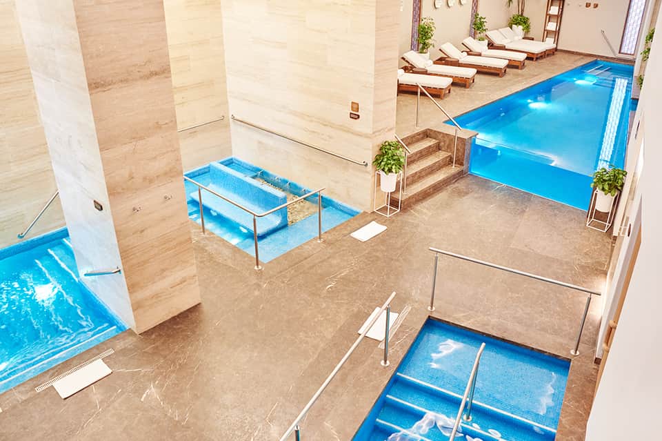 Indoor spa area with multiple hot tubs, marble columns, and heated pool facilities