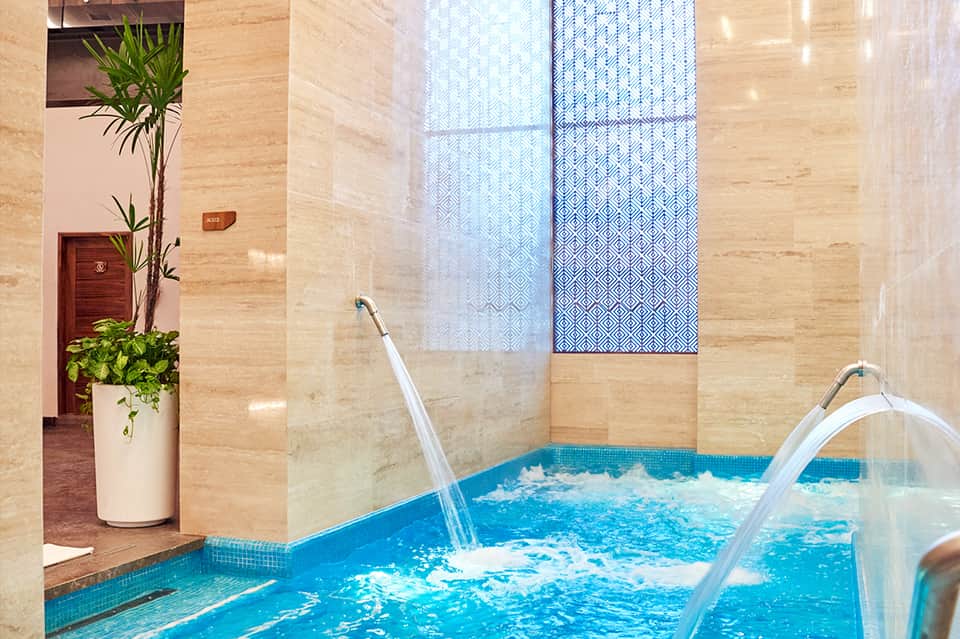 Modern indoor spa with blue tiled hot tub, geometric window patterns, and marble walls