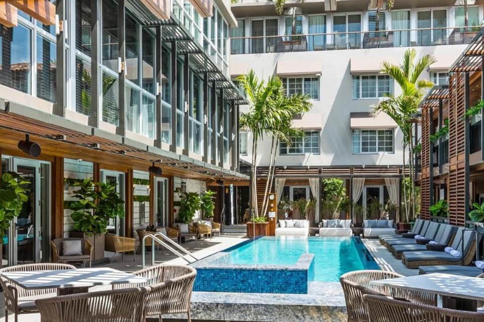 Resort courtyard pool with lounge chairs, palm trees, and contemporary building facade
