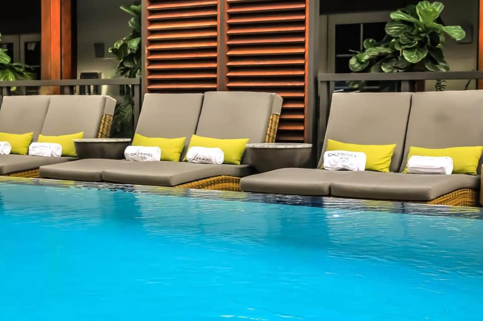 Luxury pool with submerged lounge seating, gray cushions, yellow accents, and modern architectural features
