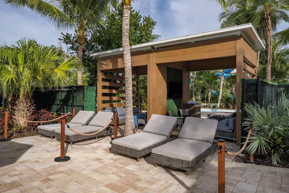 Private cabana lounge with modern wooden structure, cushioned loungers, palm trees, and resort garden views