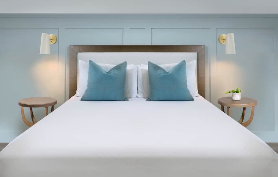 Serene hotel bedroom with light blue walls, white bedding, and teal accent pillows