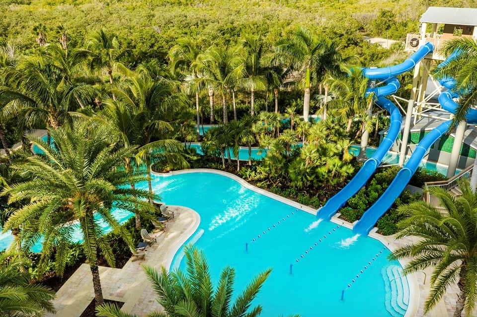 Aerial view of tropical resort pools surrounded by palm trees with blue water slides
