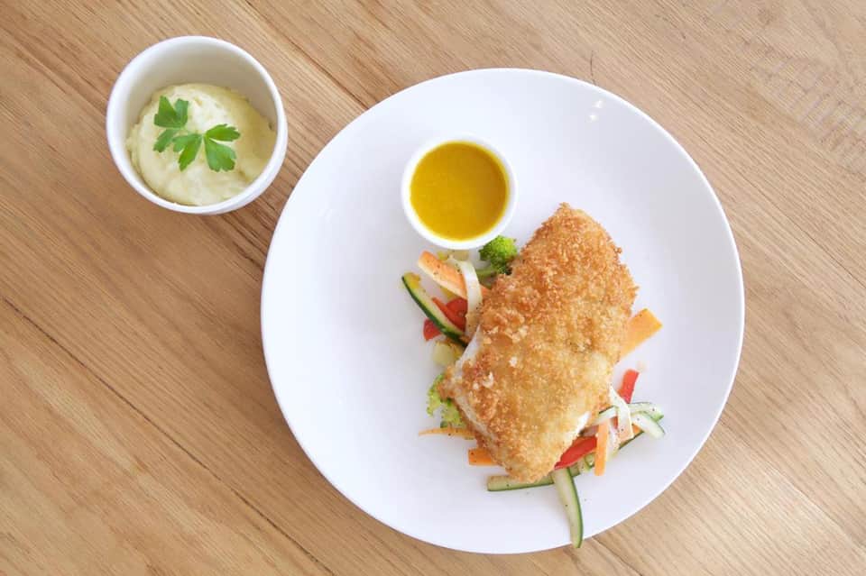Pan-seared white fish fillet with vegetable stir-fry and olive oil dip on white plate, wooden surface