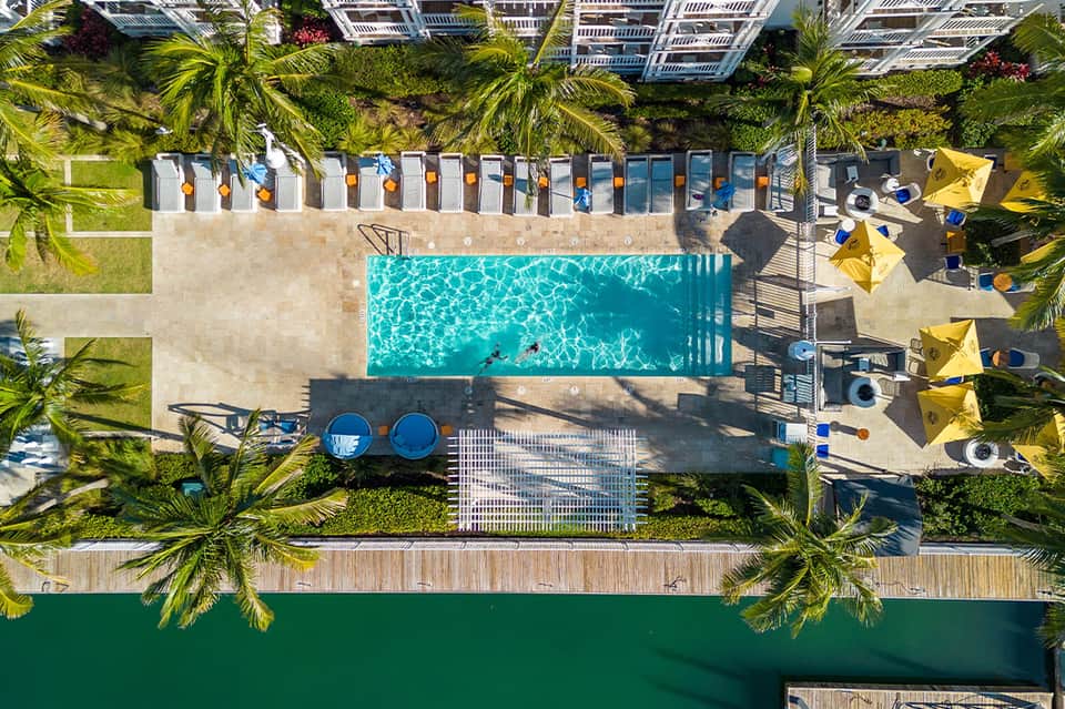Aerial view of resort pool deck with loungers, yellow umbrellas, and ocean waterfront