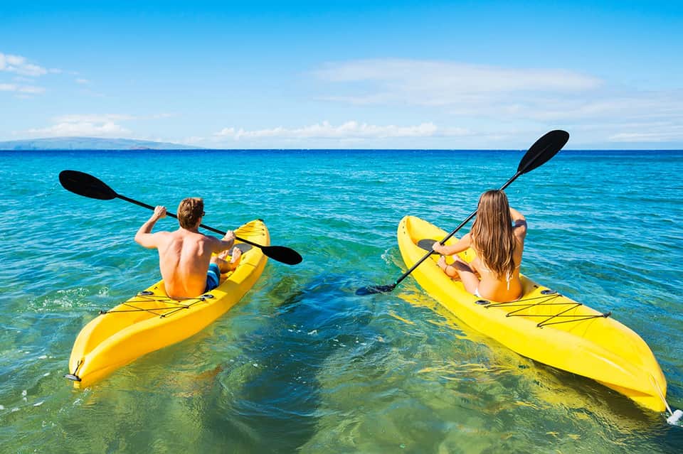 Two people kayaking in bright yellow kayaks in crystal-clear turquoise tropical ocean water