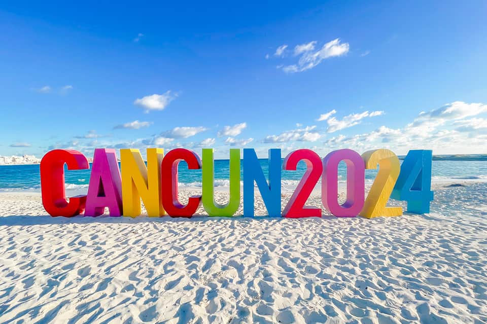 Colorful CANCUN 2024 sign on pristine sandy beach with turquoise ocean