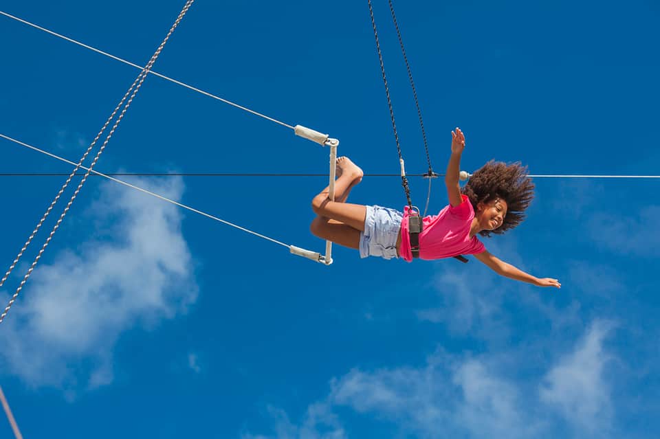 Child on zipline activity against bright blue sky over resort property