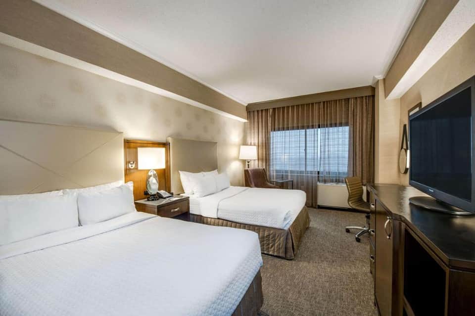 Modern hotel room with two queen beds, TV, and large window