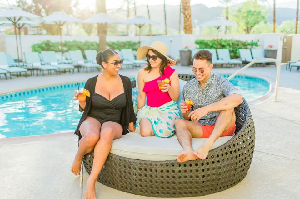 Three people sitting on woven lounge chair by resort pool with tropical mountains in background