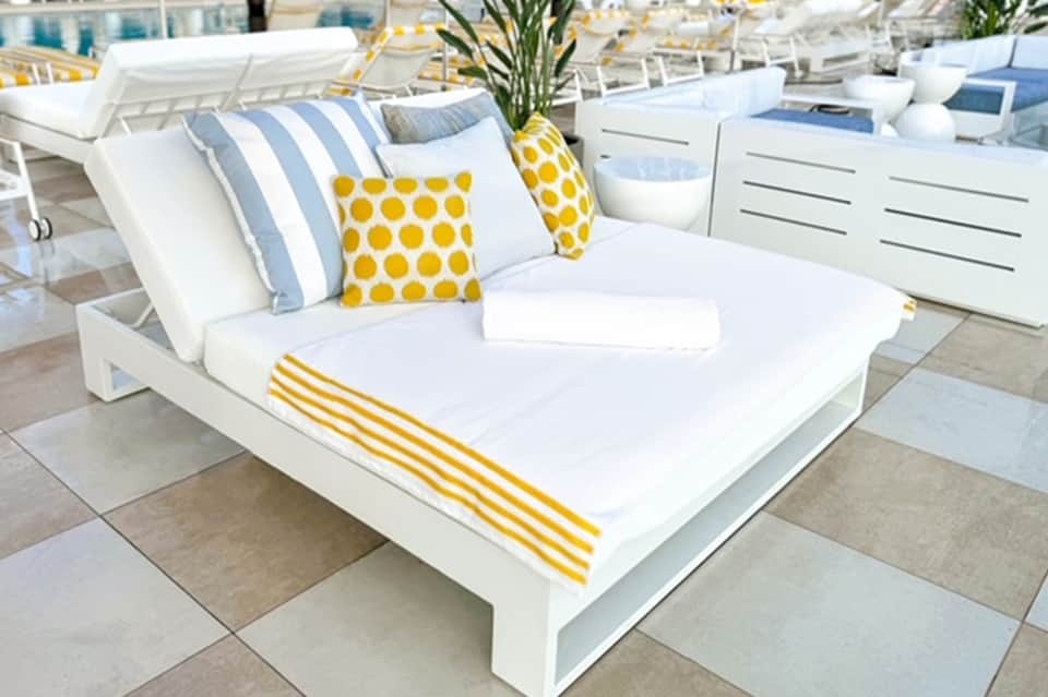 Modern white poolside daybed with yellow and gray striped pillows and décor