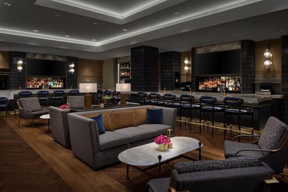 Luxury hotel media room with recliners, bar, multiple screens, and sophisticated decor