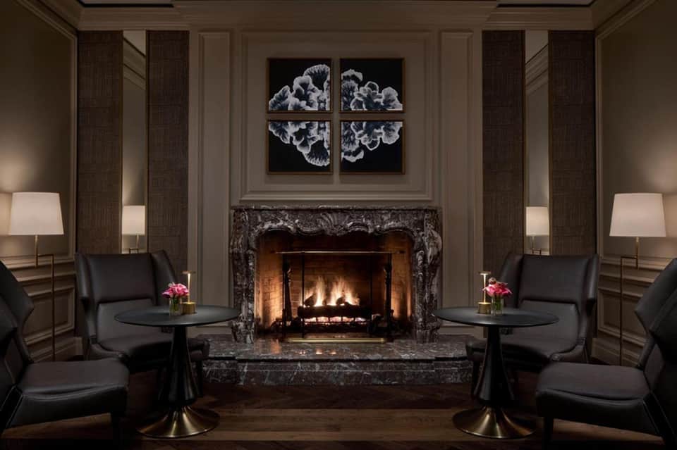 Luxury lounge with fireplace, black leather chairs, ornate marble surround, and modern art