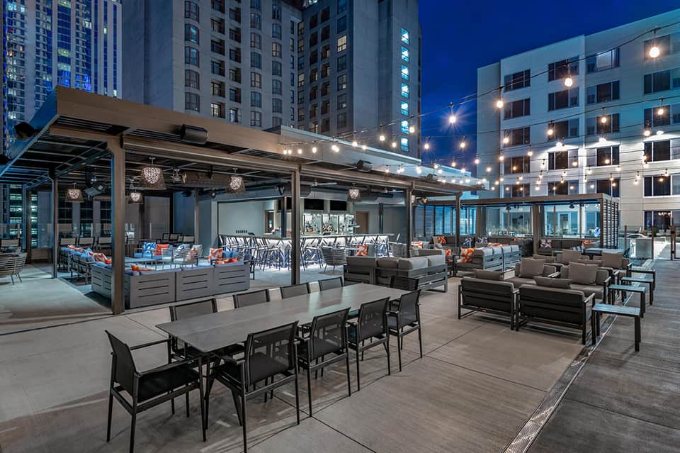 Modern rooftop terrace at dusk with dining tables, lounge seating, and city skyline